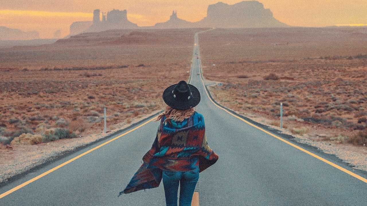 A woman walks through a desert-like landscape lacking rain.